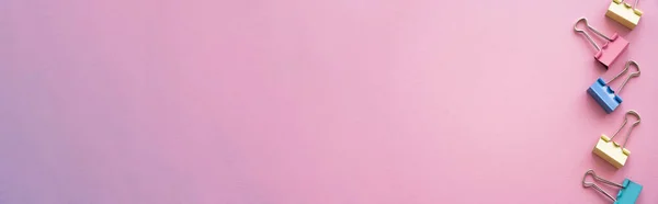 Flat lay of colorful pastel fold back clips on pink, banner — Fotografia de Stock