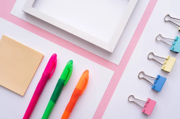 Flache Lage aus buntem Papeterie in der Nähe von leerem Rahmen und weißen Papieren auf rosa — Stockfoto