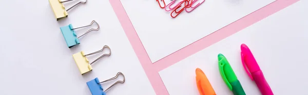 Flat lay of colorful fold back clips, paper clips and pens on white papers on pink, banner — Stockfoto