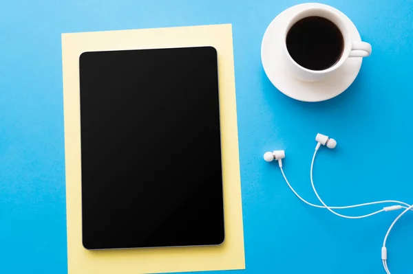 Top view of digital tablet with blank screen near cup of coffee and wired earphones on blue - foto de stock