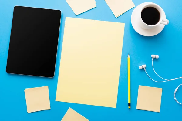 Top view of digital tablet with blank screen near cup of coffee and empty papers on blue — Fotografia de Stock