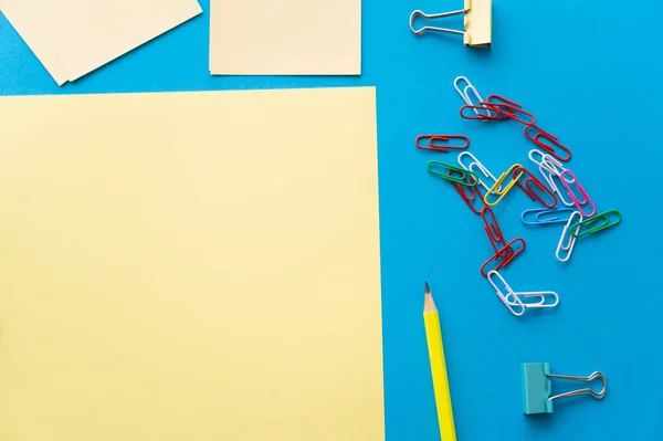 Vista superior de papéis vazios perto de clipes de papel coloridos e lápis em azul — Fotografia de Stock