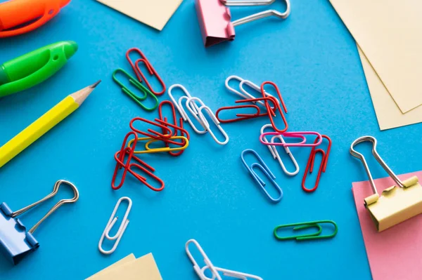 Close up view of paper notes near colorful pens and paper clips on blue — стоковое фото