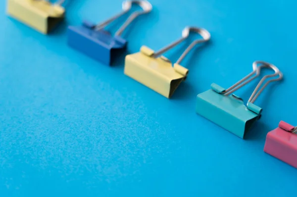 Flat lay of colorful pastel fold back clips on blue — Photo de stock