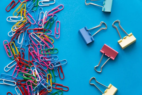 Top view of colorful paper clips and fold back clips on blue — Photo de stock