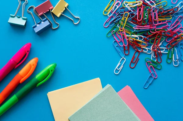 Top view of colorful paper clips and fold back clips near paper notes on blue — Photo de stock