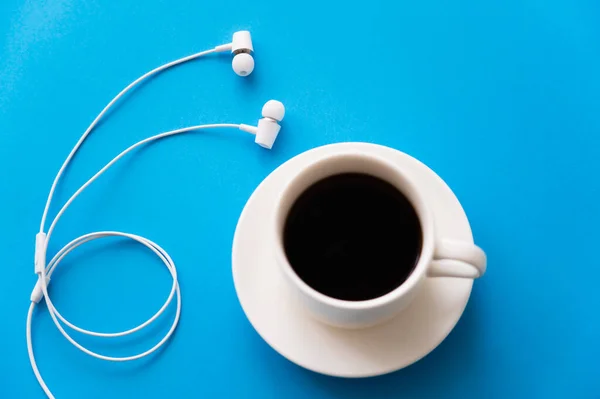 Draufsicht auf weiße kabelgebundene Kopfhörer in der Nähe einer Tasse Kaffee auf Blau — Stockfoto