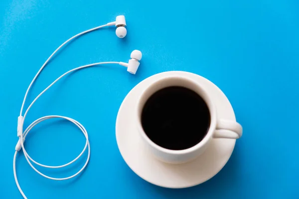 Top view of white wired earphones near cup of coffee on blue — Stock Photo