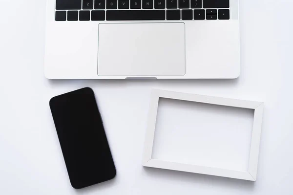 Vista dall'alto dello smartphone vicino a laptop e cornice su bianco — Foto stock