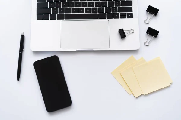 Vista superior do smartphone perto de laptop e artigos de papelaria em branco — Fotografia de Stock