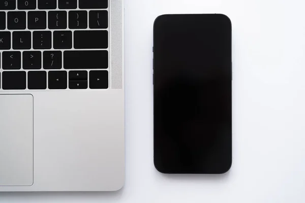 Vista dall'alto dello smartphone con schermo bianco vicino al laptop su bianco — Foto stock
