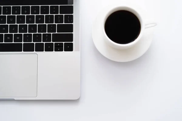 Vista superior da xícara de café perto do laptop no branco — Fotografia de Stock