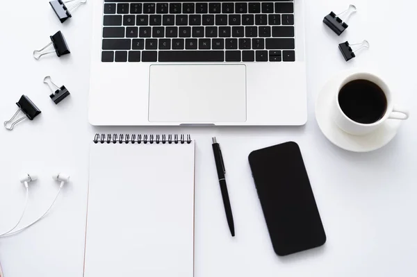 Top view of smartphone with blank screen near laptop, earphones and stationery on white — стоковое фото