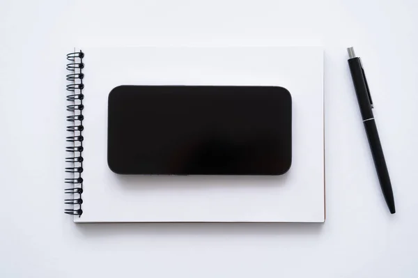 Top view of smartphone with blank screen on notebook near pen on white — Stock Photo