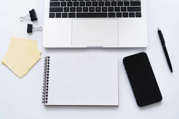 Vista dall'alto dello smartphone con schermo bianco vicino a laptop e cancelleria su bianco — Foto stock