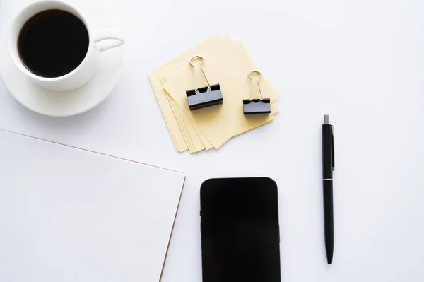Top view of mobile phone with blank screen near cup of coffee and stationery on white — Stockfoto