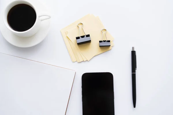 Vue du haut du téléphone portable avec écran blanc près de tasse de café et de papeterie sur blanc — Photo de stock