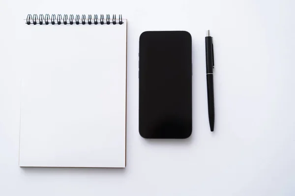 Top view of mobile phone with blank screen near notebook and pen on white - foto de stock