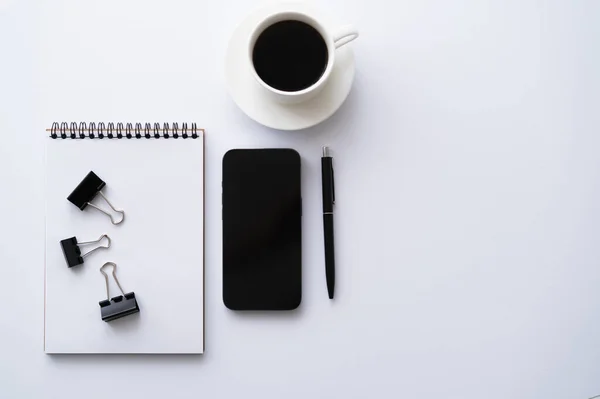 Top view of cellphone with blank screen near cup of coffee and stationery on white — стоковое фото