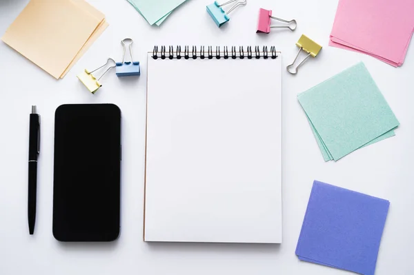 Top view of smartphone with blank screen near notebook and stationery on white — Photo de stock