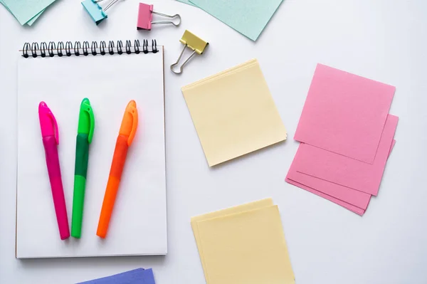 Top view of colorful pens on notebook near blank paper notes and fold back clips on white — Photo de stock