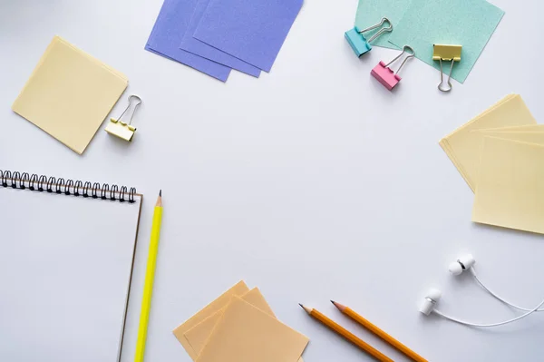 Top view of blank notebook and earphones near stationery on white — стоковое фото