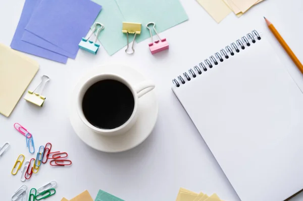 Vista superior da xícara de café perto de caderno em branco e artigos de papelaria coloridos em branco — Fotografia de Stock