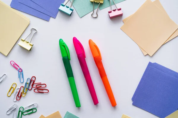 Top view of colorful pens near fold back clips and paper notes on white — Stockfoto
