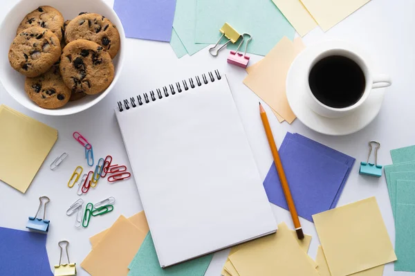 Top view of bowl with biscuits near cup of coffee and stationery on white — Stockfoto