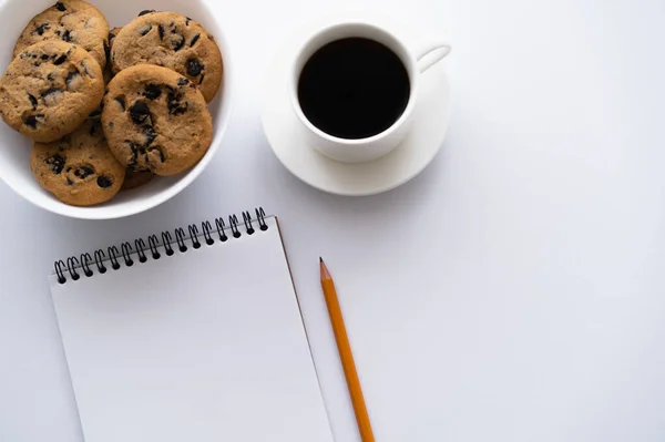 Vista superior da tigela com biscoitos com chip de chocolate perto da xícara de café e notebook em branco — Fotografia de Stock