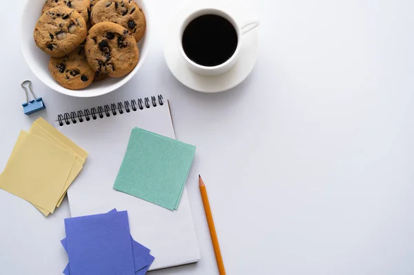 Top view of bowl with chocolate chip cookies near cup of coffee and stationery on white - foto de stock