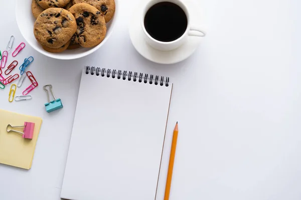 Vista superior da xícara de café, biscoitos e artigos de papelaria perto do smartphone com tela em branco no branco — Fotografia de Stock