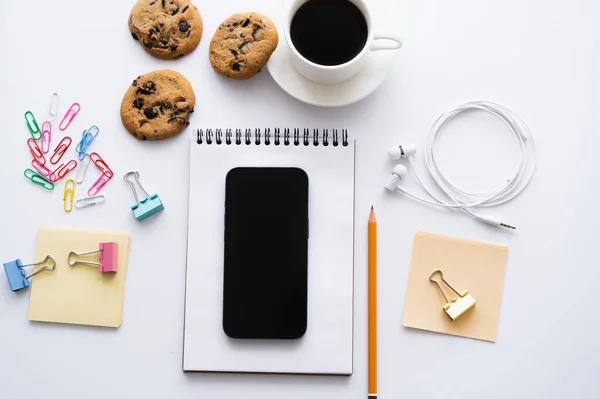 Vista superior de la taza de café, galletas y teléfono inteligente con pantalla en blanco cerca de papelería en blanco - foto de stock