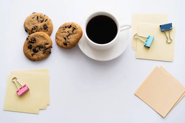 Draufsicht auf Tasse Kaffee und Schokoladenkekse in der Nähe von Schreibwaren auf Weiß — Stockfoto