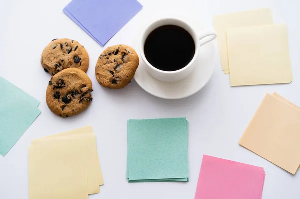 Vista superior de galletas de chispas de chocolate y taza de café cerca de notas de papel en blanco - foto de stock