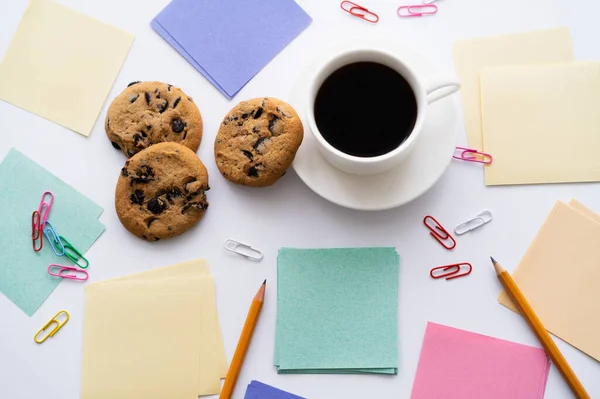 Draufsicht auf Schokoladenkekse und Tasse Kaffee in der Nähe von Schreibwaren auf Weiß — Stockfoto