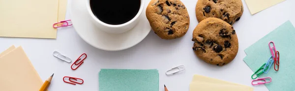 Draufsicht auf Schokoladenkekse und Tasse Kaffee in der Nähe von Schreibwaren auf weiß, Banner — Stockfoto