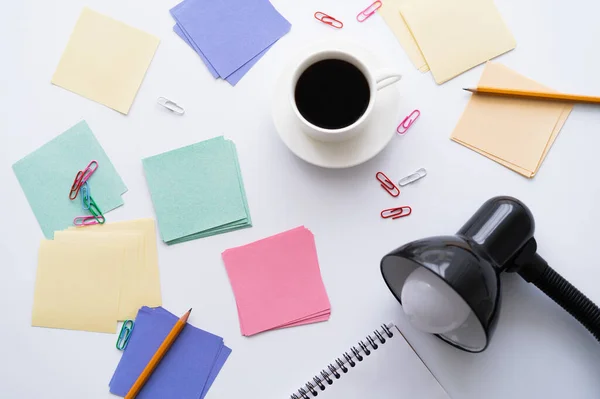 Top view of cup of coffee near stationery and lamp on white — Stock Photo