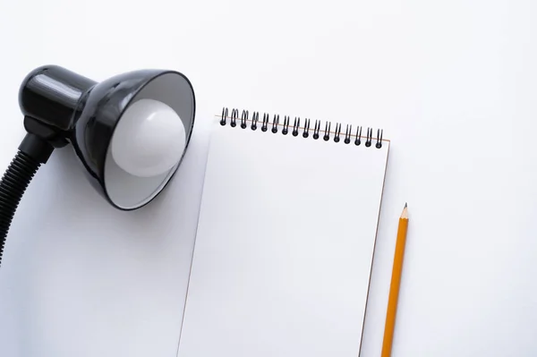 Top view of blank notebook near pencil and lamp on white - foto de stock