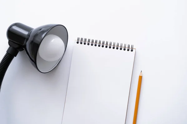 Top view of blank notebook near pencil and lamp on white — Stock Photo