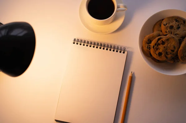 Top view of lamp near chocolate chip cookies, cup of coffee and notebook on white — Stock Photo