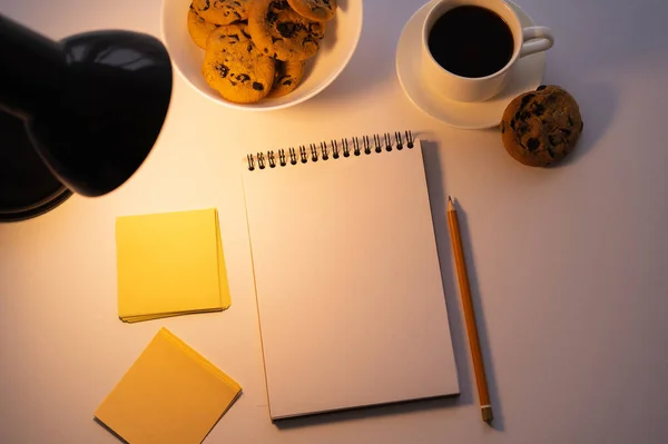 Vue du dessus des cookies aux pépites de chocolat lampe, tasse de café et bloc-notes vierge sur blanc — Photo de stock