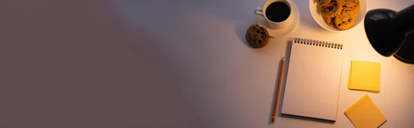 Vista superior de las galletas de la viruta del chocolate de la lámpara, taza de café y cuaderno en blanco en blanco, bandera - foto de stock