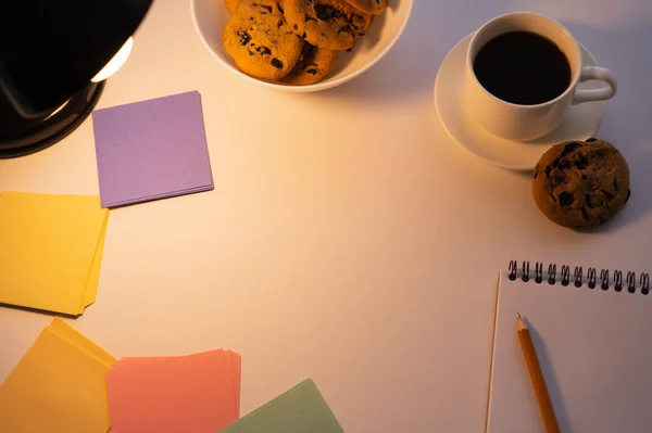 Top view of lamp near chocolate chip cookies, cup of coffee and blank paper notes on white — Fotografia de Stock