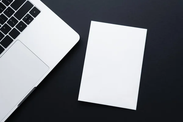 Top view of blank paper near laptop on black — Stock Photo