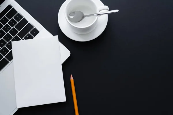 Vue du dessus du papier blanc sur ordinateur portable près du crayon et tasse vide avec cuillère sur noir — Photo de stock