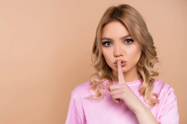 Mujer seria con el pelo ondulado mostrando signo de silencio aislado en beige - foto de stock