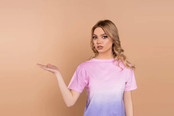 Discouraged woman with wavy hair pointing with hand isolated on beige — Stockfoto