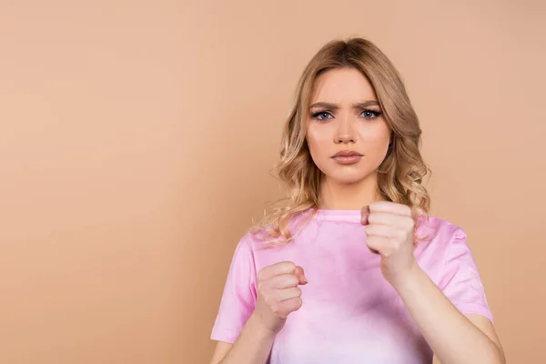 Mujer irritada mirando a la cámara y mostrando puños cerrados aislados en beige - foto de stock