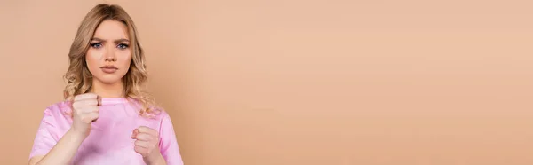 Femme en colère regardant la caméra et montrant les poings serrés isolés sur beige, bannière — Photo de stock